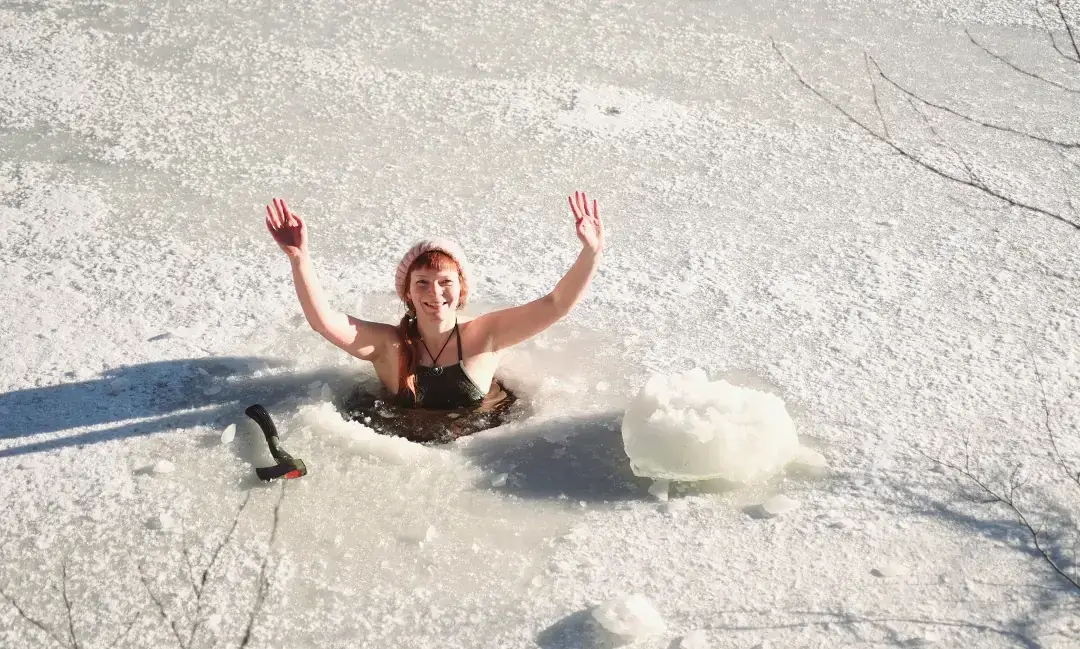 Frau streckt jubelnd die Arme aus einem Eisloch in einem zugefrorenen See