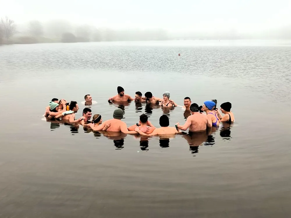 Gruppe von Eisbadern steht im Kreis in einem nebligen Winter-See beim gemeinsamen Eisbad